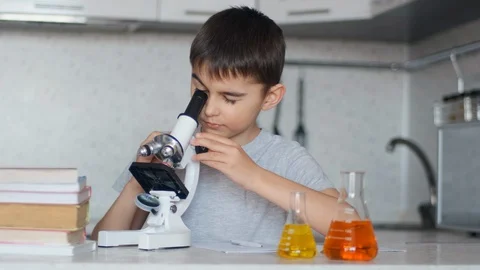 A boy learns chemistry using a microscope and makes notes in a notebook Stock Footage 127942137
