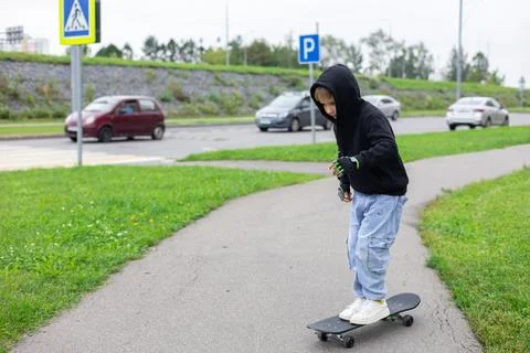 A boy learns to skateboard on a city sidewalk. A hipster boy kicks off and Stock Photos
