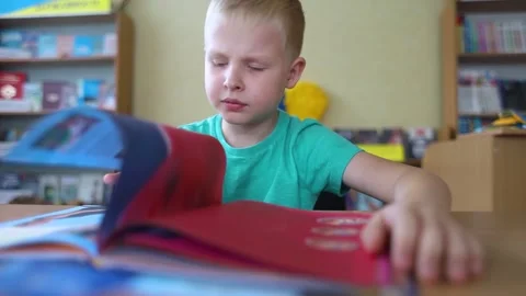 Boy in library. Seven year Ukrainian guy is sitting at a table in library and re Stock-Footage 247695637