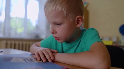 Boy in library. Seven year Ukrainian guy is sitting at a table in library and re Video stock 247695699