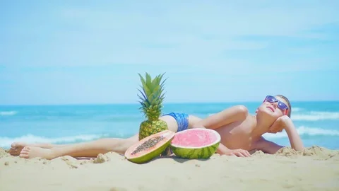Boy lies on the beach with a composition of exotic fruits against the sea. Stock Footage 111508121