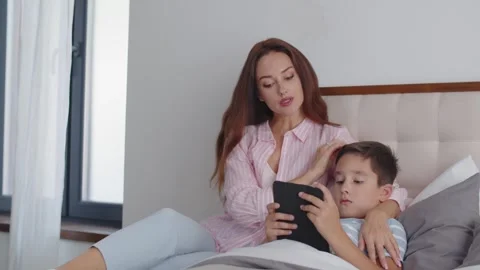 A boy lies on the bed and gets ready to sleep, reading an ebook on a tablet. A Stock Footage 255050140