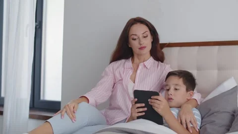 A boy lies on the bed and gets ready to sleep, reading an ebook on a tablet. A Stock Footage 255306047
