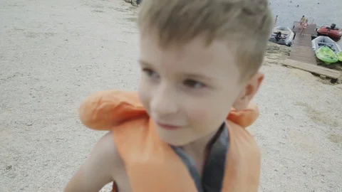 A boy in a life jacket grimaces on the shore Stock Footage 94346259