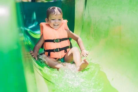 A boy in a life jacket slides down from a slide in a water park Stock Photos