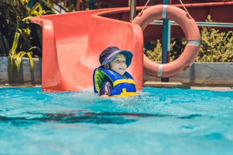 A boy in a life jacket slides down from a slide in a water park Fotos Stock