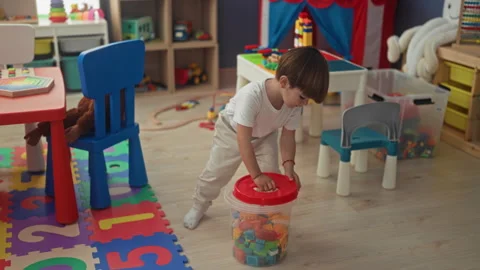Boy lifting tub of blocks at red table, hand reaching toward toy sink in a .. Stock Footage 339247340