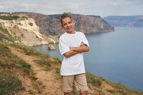 A boy in light clothes against the background of a beautiful seascape smiles wit Stock Photos