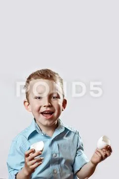 Boy in a light shirt holding a shell from the egg and smiling on a light back Stock Photos
