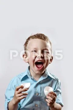 Boy in a light shirt holding a shell from the egg and smiling on a light back Stock Photos