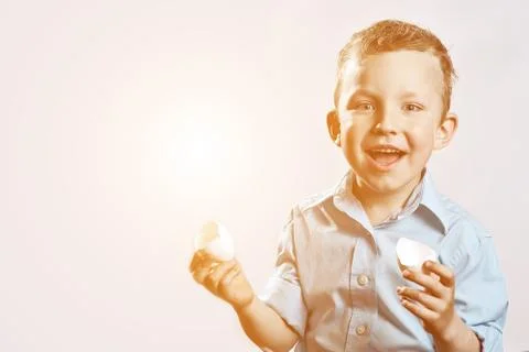 Boy in a light shirt holding a shell from the egg and smiling on a light back Photos