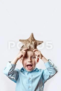 Boy in a light t-shirt holding a starfish on a white background Stock Photos