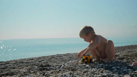 A boy loads rocks on the beach into the back of a toy truck Stock Footage 229276640