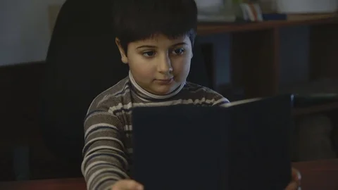 The boy is looking at the book sitting at the table Stock Footage 75558120