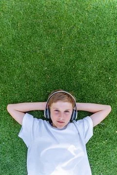 Boy looking at camera while listening music with headphones lying on grass Foto stock