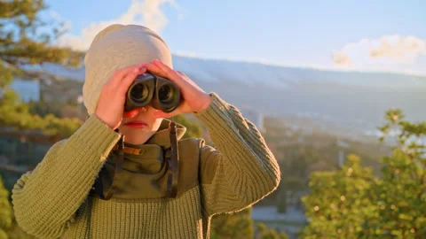 Boy looking directly into camera through binoculars outdoors Video stock 329770013