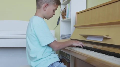 Boy looking down, practicing piano with sheet music, skill, talent, musical Stock Footage 155480132
