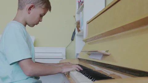 Boy looking down, practicing piano with sheet music, skill, talent, musical Stock Footage 155484863