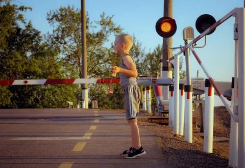 Boy is looking forward to approaching the train at the railway crossing with  Stock Photos