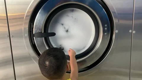 Boy looking at an industrial washing machine with a round viewing window Stock Footage 346360184