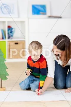Boy looking at mother drawing on chart paper Stock Photos