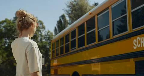 Boy looking out schoolbus window waving to mom. Mother sending air-kiss to son. Stock Photos