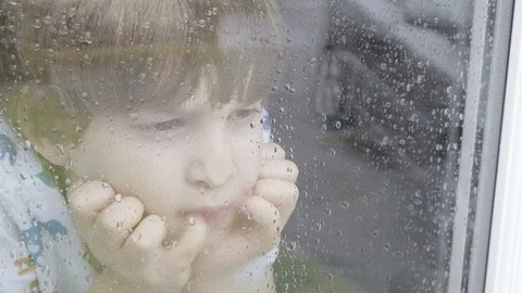 Boy looking out of window on a rainy day 스톡 동영상 129335754