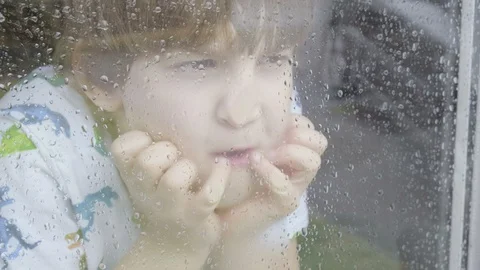 Boy looking out of window on a rainy day 스톡 동영상 129338467
