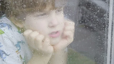 Boy looking out of window on a rainy day Stock Footage 129341957