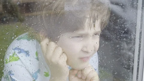 Boy looking out of window on a rainy day Stock Footage 129345559