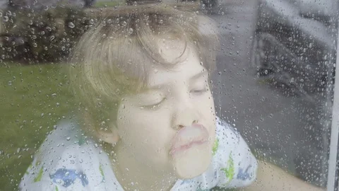 Boy looking out of window on a rainy day Video stock 129345882