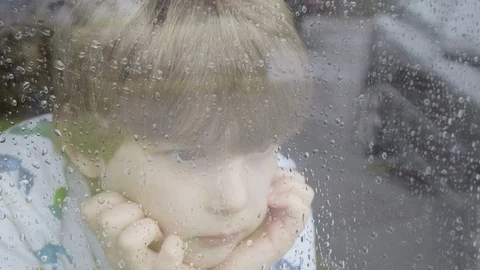 Boy looking out of window on a rainy day Stock Footage 129346131
