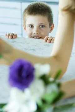 Boy looking over edge of counter, woman and flowers in blurred foreground Stock Photos