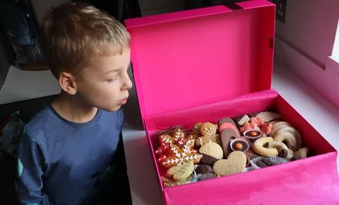 A boy is looking into a pink box full of cookies Stock Photos