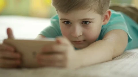  Boy looking at a smart phone lying on his side. Stock Footage 72870123
