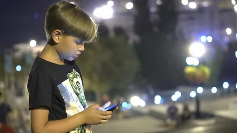 The boy is looking at the smartphone in the background of the night city. Close 動画素材 79274271