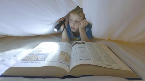 Boy looking through a large book under a duvet Stock Footage 96317633