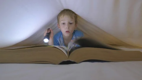 Boy looking through a large book under a duvet Stock Footage 96319992