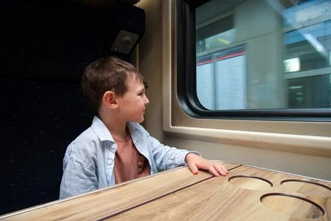Boy looking through train window during trip. Small kid sitting at table in.. Stock Photos