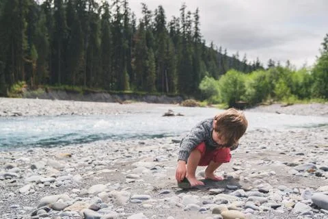 Boy looking under a rock in a river bed Stock Photos
