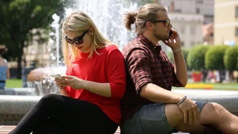 Boy looks angry while speaking with someone on cellphone and leaning on his girl Stock Footage 77485283