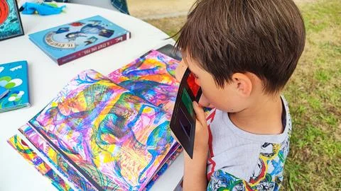 A boy looks at a multi-colored book through 3D glasses. Foto stock