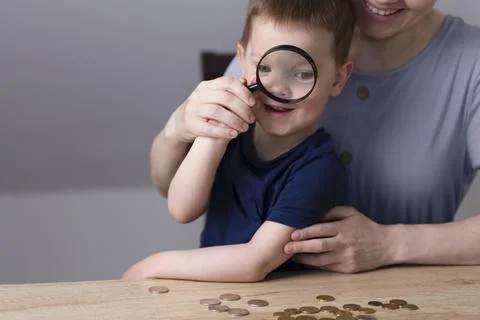 The boy looks with one eye through a magnifying glass and laughs. Stock Photos