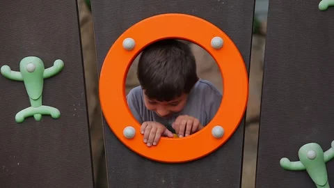 A boy looks out of a round window on a children's playground Stock Footage 266170386