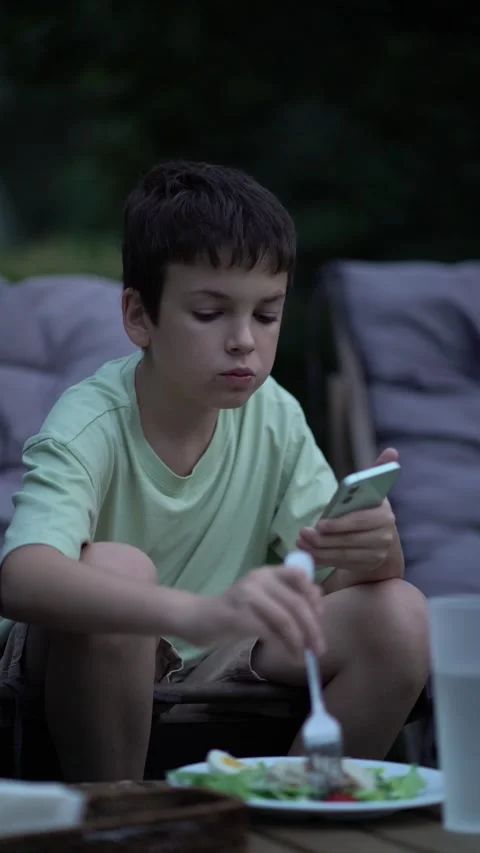 Boy looks at smartphone while eating Caesar salad in outdoor restaurant. Stock-Footage 342968600