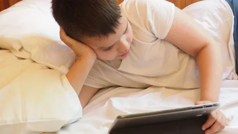 Boy looks at the tablet in the evening or at night before going to bed 動画素材 191564497