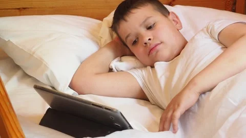 Boy looks at the tablet in the evening or at night before going to bed Stock Footage 191564584