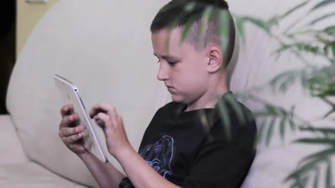Boy looks at the tablet holding it in his hands and presses something Stock Footage 199784093
