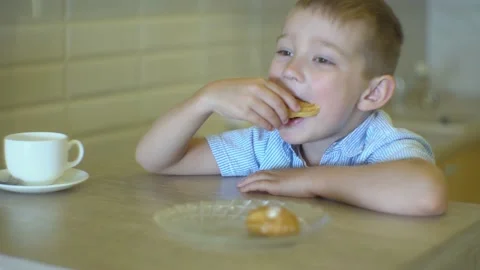 The boy looks thoughtfully out the window and eats eclair Video stock 168074322