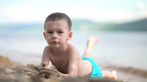 Boy lying on beach sand, looking at camera with sand-covered hands Stock-Footage 338415587